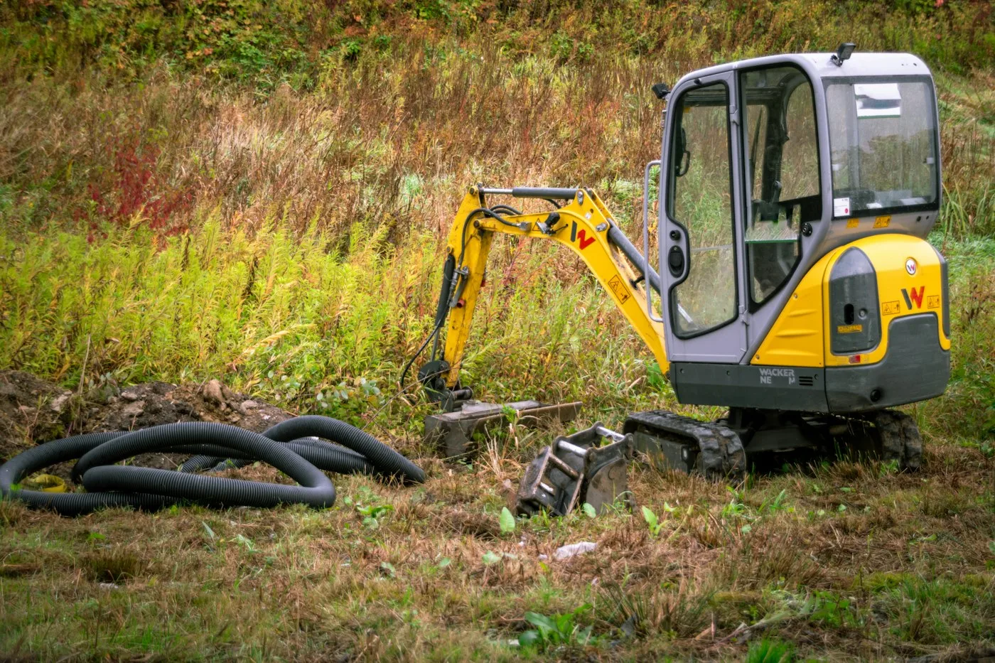 Compact excavator beside grass and hoses